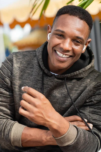 Retrato de hombre afroamericano feliz en auriculares inalámbricos sonriendo al aire libre - foto de stock