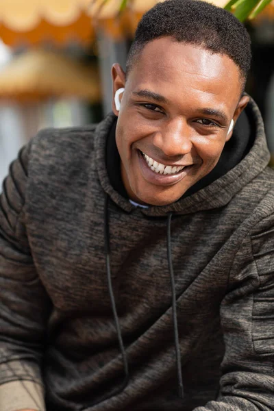Porträt eines fröhlichen afrikanisch-amerikanischen Mannes mit drahtlosen Kopfhörern, der im Freien lächelt — Stockfoto
