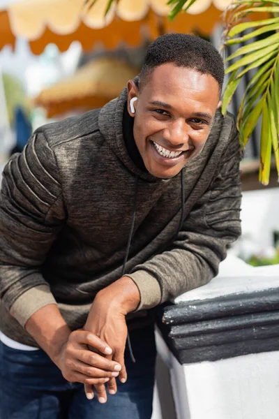Fröhlicher afrikanisch-amerikanischer Mann mit drahtlosem Kopfhörer, der im Freien lächelt — Stockfoto
