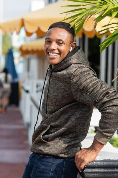 Erfreut afrikanisch-amerikanischer Mann mit drahtlosem Kopfhörer, der in der Nähe von Outdoor-Bistro steht — Stockfoto