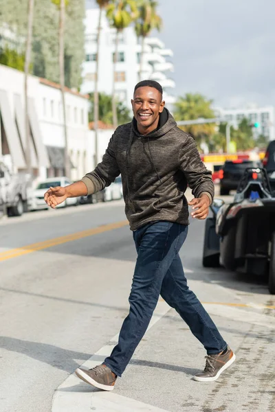 Pleine longueur de joyeux homme afro-américain en sweat à capuche et jeans marchant dans la rue à Miami — Photo de stock