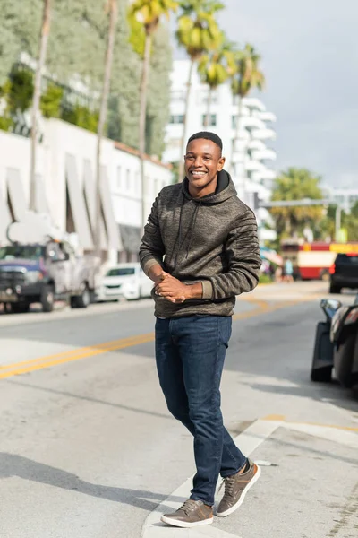 Piena lunghezza di piacere afroamericano uomo in felpa con cappuccio e jeans a piedi per strada a Miami — Foto stock