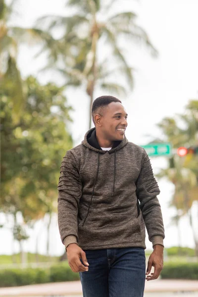 Heureux homme afro-américain en sweat à capuche et jeans marchant dans la rue à Miami — Photo de stock