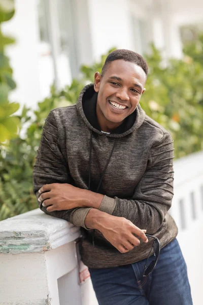 Satisfied african american man in hoodie and jeans holding sunglasses outdoors — Stock Photo
