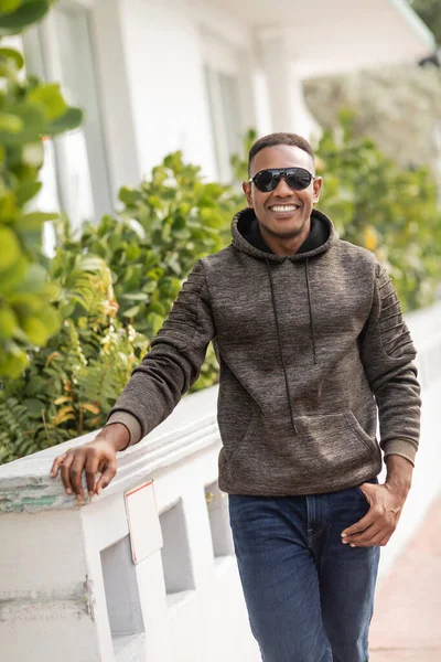 Позитивний афроамериканський чоловік в светрі і стильних сонцезахисних окулярах, що стоять на відкритому повітрі — стокове фото