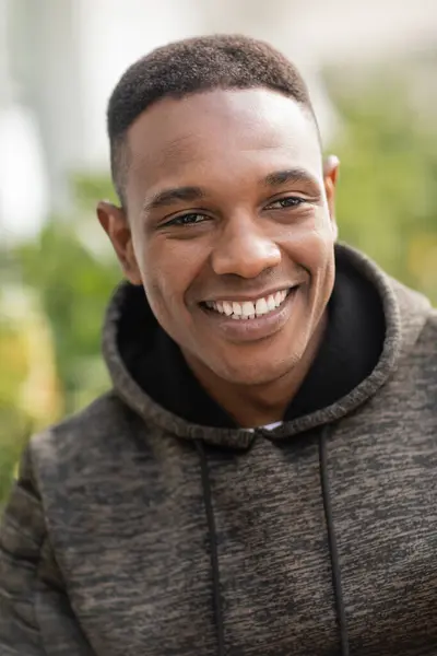 Portrait of positive african american man in hoodie smiling outdoors — Stock Photo