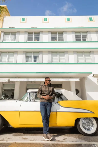 MIAMI, FLORIDA, USA - DECEMBER 15, 2022: happy african american man in sunglasses standing near vintage yellow car — Stock Photo