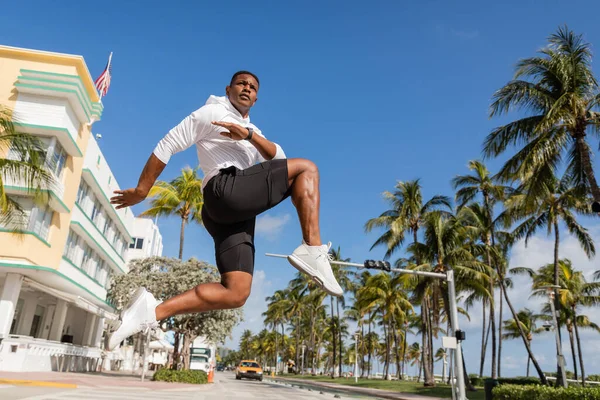Esportivo homem americano africano pulando ao lado de palmeiras e condomínio moderno em Miami — Fotografia de Stock