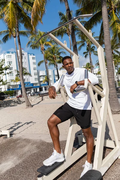 Full length of african american sportsman working out on outdoor gym equipment in Miami beach — Stock Photo