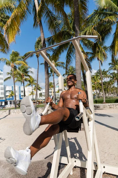 Sportif afro-américain torse nu faisant de l'exercice sur un équipement de gymnastique en plein air à Miami Beach — Photo de stock