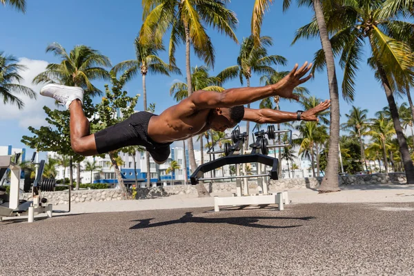 Shirtless african american sportsman falling on ground next to palm trees in Miami beach — Stock Photo