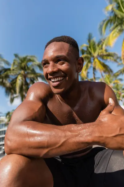 Retrato del sudoroso y feliz deportista afroamericano sin camisa mirando hacia otro lado después del entrenamiento - foto de stock