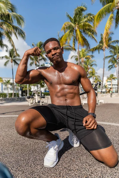 Strong african american sportsman in shorts and sneakers showing muscles after workout in Miami beach — Stock Photo