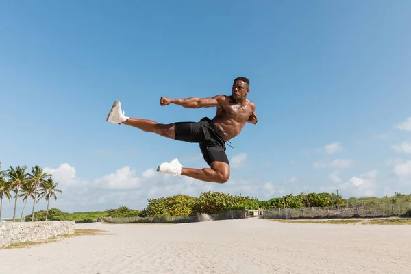 Muscular afro-americano homem pulando enquanto trabalhava na praia de Miami — Fotografia de Stock