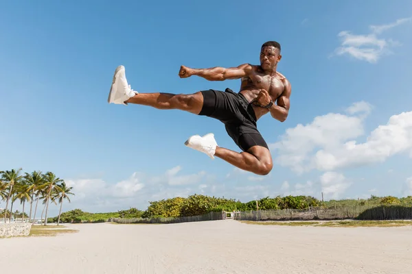 Muscular african american man jumping while exercising in Miami beach — Stock Photo