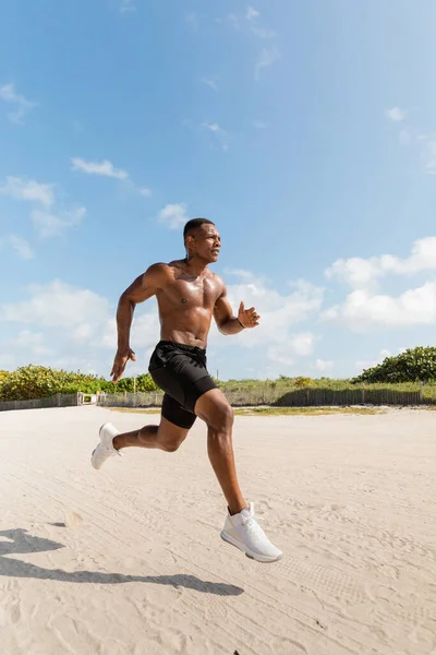 Sportlicher und hemdsloser afrikanisch-amerikanischer Mann in kurzen Hosen beim Laufen auf Sand in Miami — Stockfoto