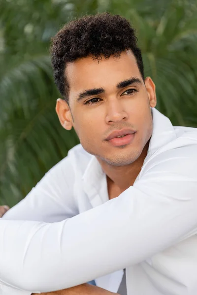 Portrait of young and handsome curly cuban man in modern white shirt looking away, vacation in Miami — Stock Photo
