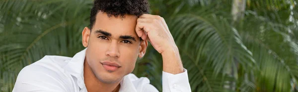 Retrato del relajado hombre cubano de camisa blanca cogido de la mano cerca de la cabeza en Miami, playa sur, pancarta - foto de stock