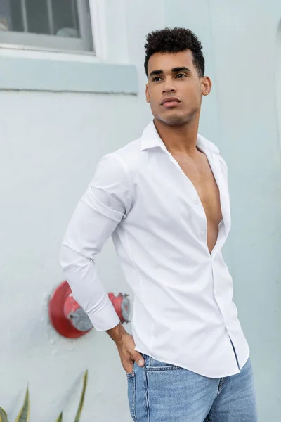 Fiducioso giovane cubano in camicia bianca in posa mentre tiene la mano in tasca di jeans a Miami — Foto stock