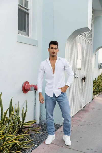 Piena lunghezza di giovane cubano in camicia elegante e jeans blu in posa per strada a Miami — Foto stock