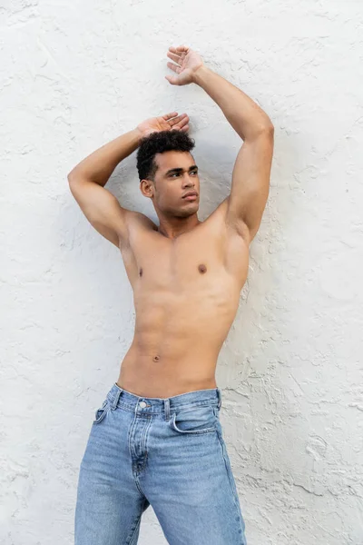 Muskulöser und gut aussehender junger Mann in blauen Jeans posiert in der Nähe der weißen Mauer auf der Straße in Miami — Stockfoto