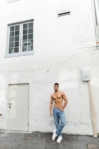 Full length of muscular and shirtless cuban man in blue jeans posing near building in Miami — Stock Photo
