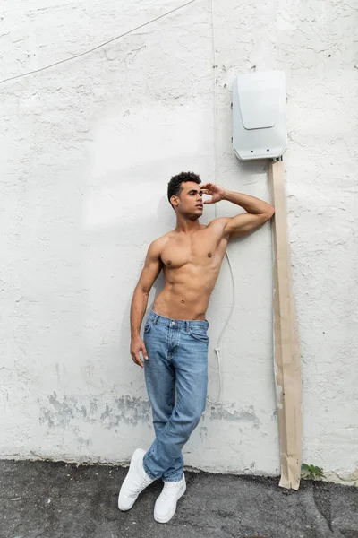 Shirtless cuban man in jeans standing near wire on white wall in Miami during summer, muscular — Stock Photo