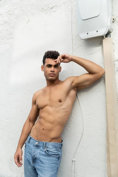 Jeune homme cubain athlétique en jeans bleus posant près du bâtiment à Miami, mur blanc — Photo de stock