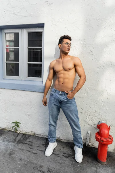 Comprimento total de sexy muscular cubano homem em forma redonda óculos e jeans posando e olhando para longe — Fotografia de Stock