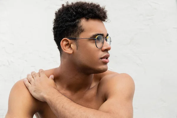 Молодой кубинский мужчина без рубашки в модных круглых очках касается плеча и отворачивается — стоковое фото