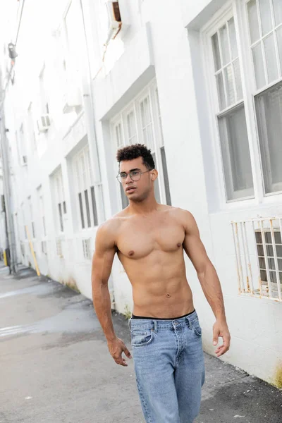 Shirtless sexy cuban man in round-shaped eyeglasses and jeans looking away while walking in Miami — Stock Photo