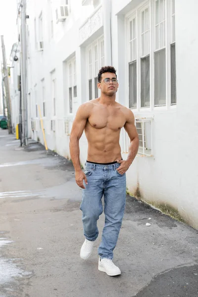 Sexy cuban man in round-shaped eyeglasses and jeans looking away while walking in Miami — стоковое фото