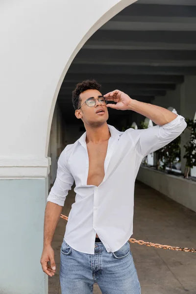Sexy jeune homme cubain en chemise blanche et jeans touchant lunettes de vue de forme ronde à Miami — Photo de stock