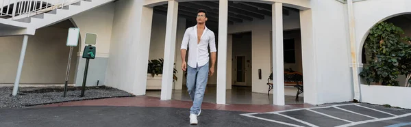 Jeune homme cubain à la mode en lunettes, jeans bleus et chemise blanche marchant près du bâtiment, bannière — Photo de stock