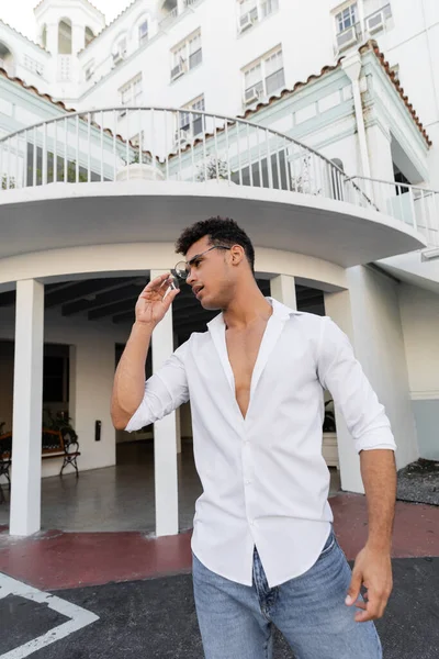 Hombre cubano relajado en camisa blanca y jeans con elegantes gafas redondas en Miami - foto de stock