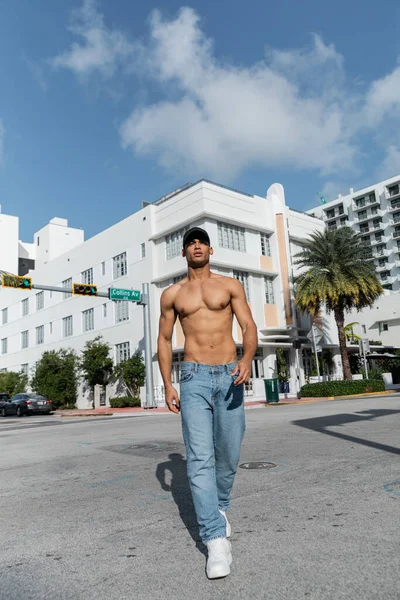 Jovem cubano sem camisa em jeans e boné de beisebol andando na rua urbana em Miam, durante o verão — Fotografia de Stock