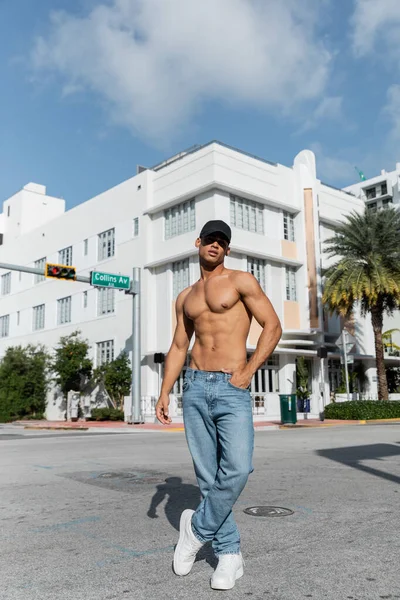 Sem camisa sexy cubano homem em jeans e boné de beisebol andando na rua urbana em Miam, verão — Fotografia de Stock