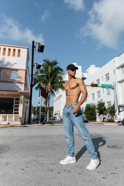 Homem cubano com corpo atlético em boné de beisebol e jeans azuis na rua em Miami, na praia sul — Fotografia de Stock