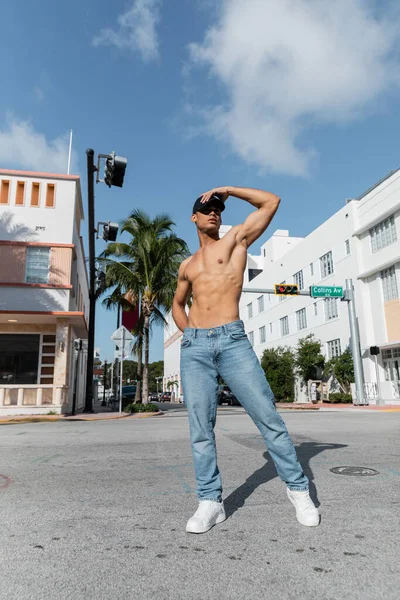 Homem cubano quente com corpo atlético em boné de beisebol e jeans azuis na rua em Miami, praia sul — Fotografia de Stock