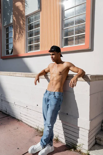 Sexy homme cubain torse nu avec corps athlétique en casquette de baseball et jeans debout dans la rue à Miami — Photo de stock