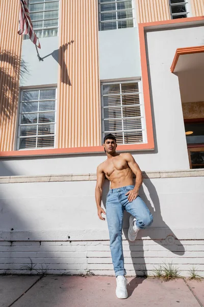 Homme cubain sexy avec corps athlétique en casquette de baseball et jeans debout dans la rue à Miami — Photo de stock