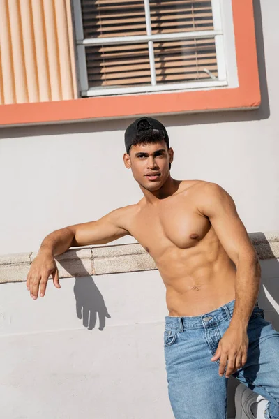 Uomo cubano muscoloso con corpo atletico in berretto da baseball e jeans in piedi in strada a Miami — Foto stock