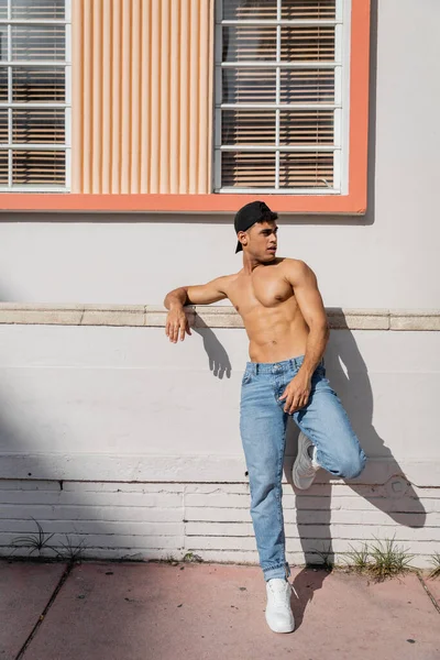 Homem cubano sexy com corpo muscular em boné de beisebol e jeans de pé na rua em Miami — Fotografia de Stock