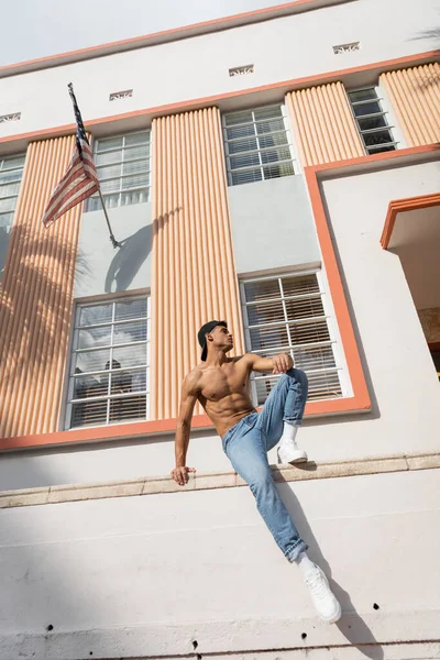 Кубинский мужчина с мускулистым телом позирует в бейсболке и джинсах на улице в Майами летом — стоковое фото