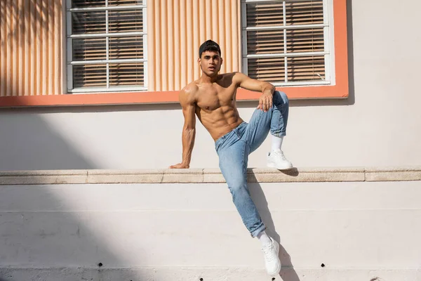 Кубинский мужчина с мускулистым телом позирует в бейсболке и джинсах на улице в Майами летом — стоковое фото