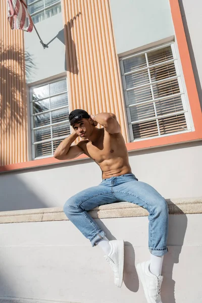 Athletic and good looking cuban man in blue jeans and sneakers touching baseball cap in Miami — Stock Photo