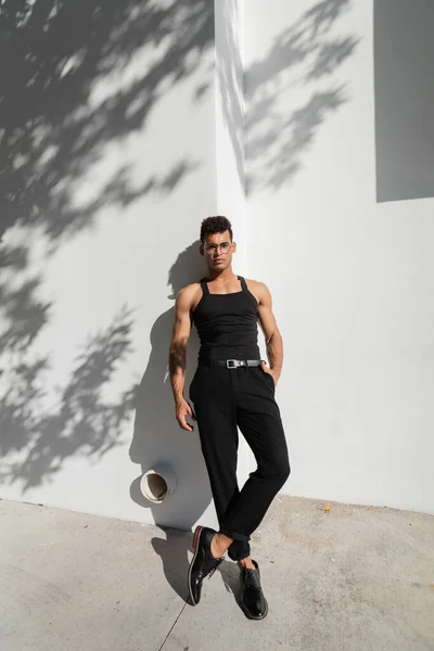 Jeune homme cubain branché posant près du mur blanc avec ombre sur la rue urbaine de Miami, plage sud — Photo de stock