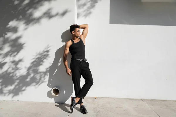 Sexy cuban man in eyeglasses and black sleeveless t-shirt posing near wall in Miami, during summer — стоковое фото