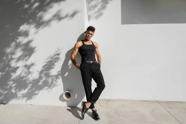 Homem quente em óculos e t-shirt preto sem mangas posando perto da parede em Miami, durante o verão — Fotografia de Stock