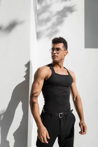 Young cuban man in eyeglasses standing near building with shadow on street in Miami, south beach — Stock Photo